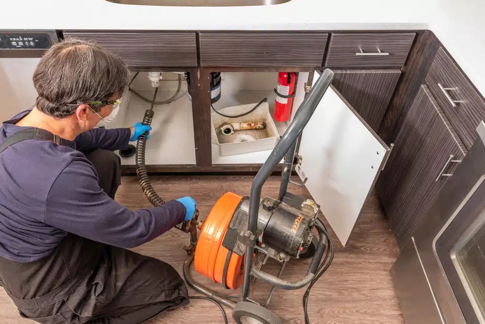 Plumber clearing a kitchen drain with an auger